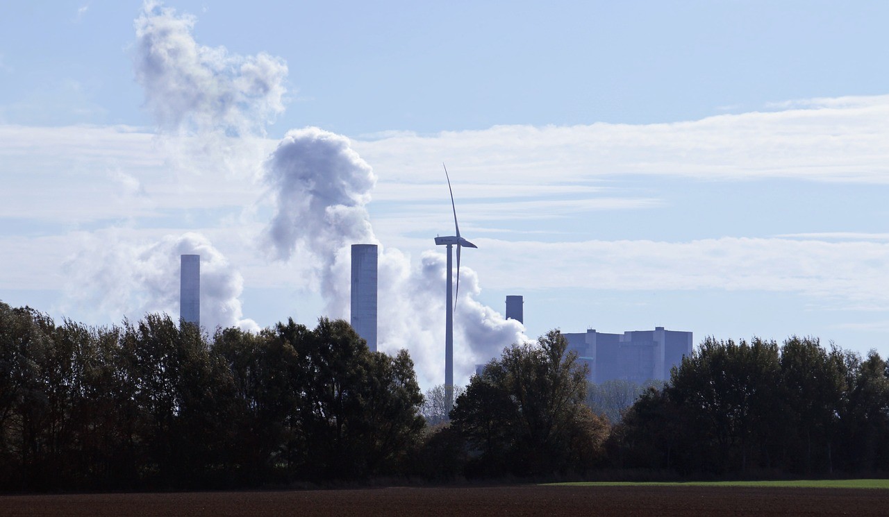 Zdjęcie poglądowe turbiny wiatrowej na tle elektrowni węglowej
